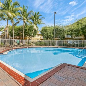Pool Area With Brick Style Deck, Sun Chairs, And Palm Trees